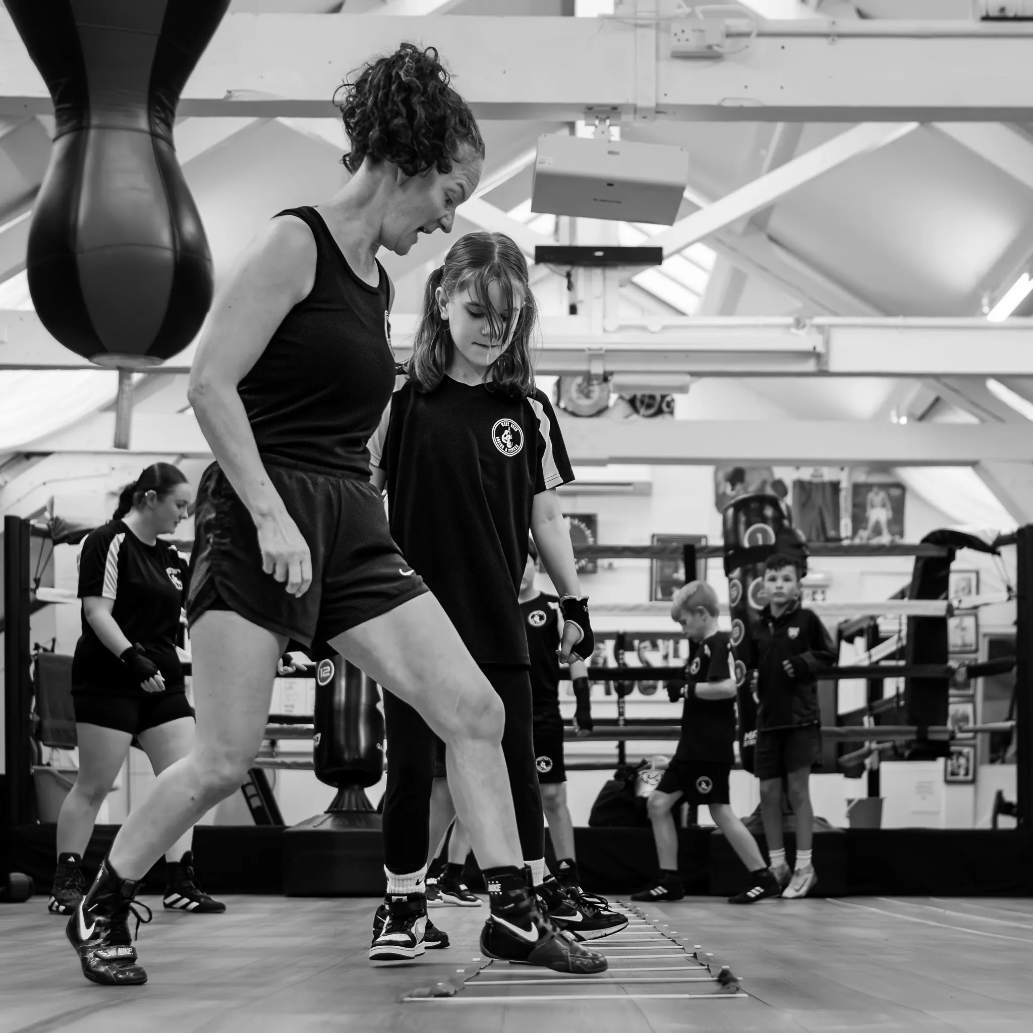 A female instructor and a young student practicing agility ladder drills on the gym floor at West Oxon Boxing & Fitness.