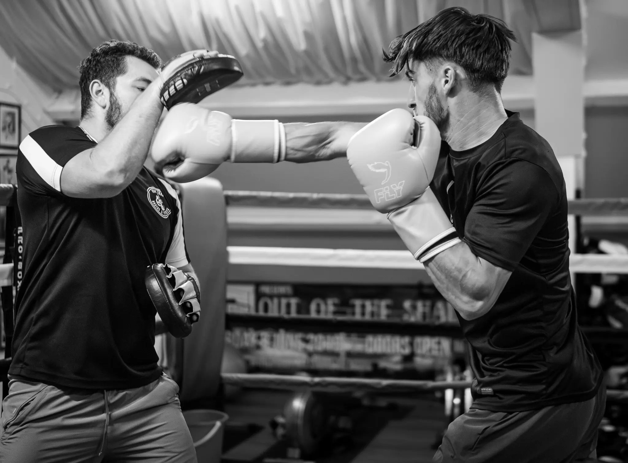 Competitive Boxing Training & Coaching A boxing coach wearing focus mitts catches a powerful jab from a student during a training session in the ring.