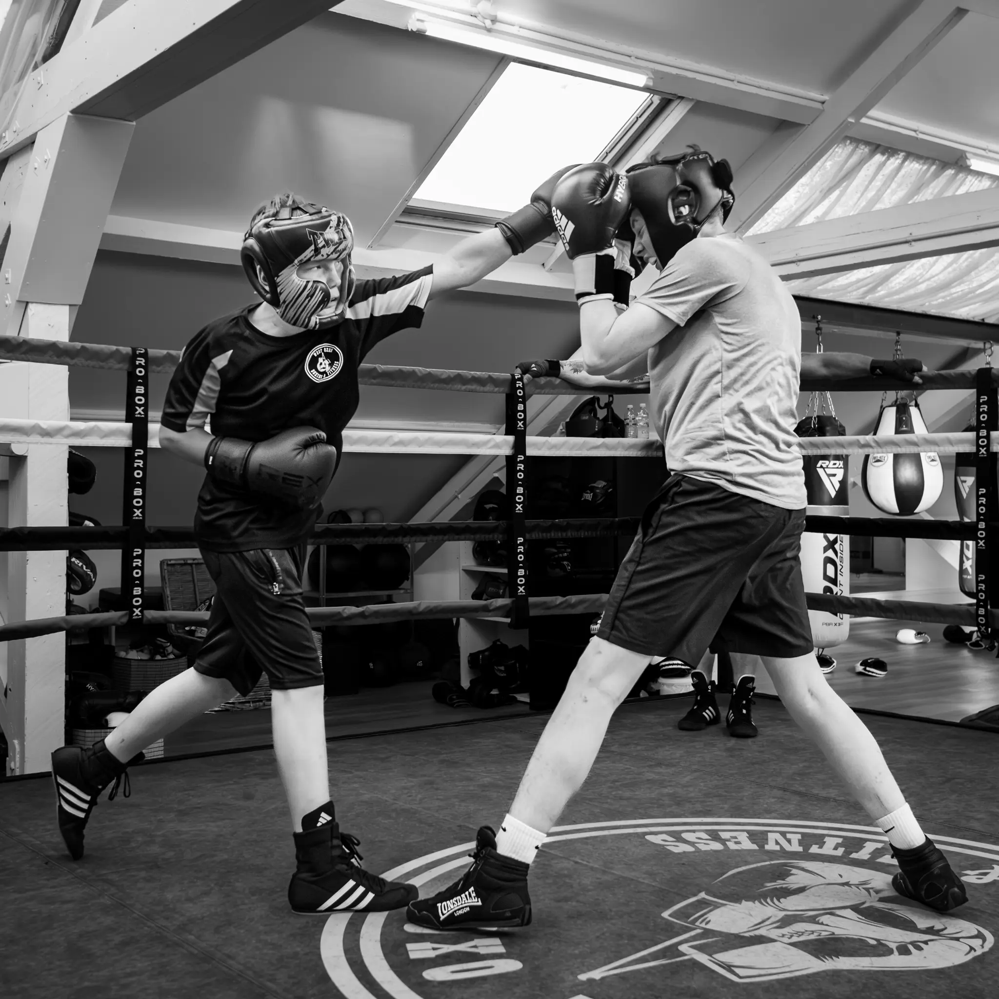 Two teen boxers in headguards and gloves practicing technical sparring inside a boxing ring at West Oxon Boxing & Fitness.