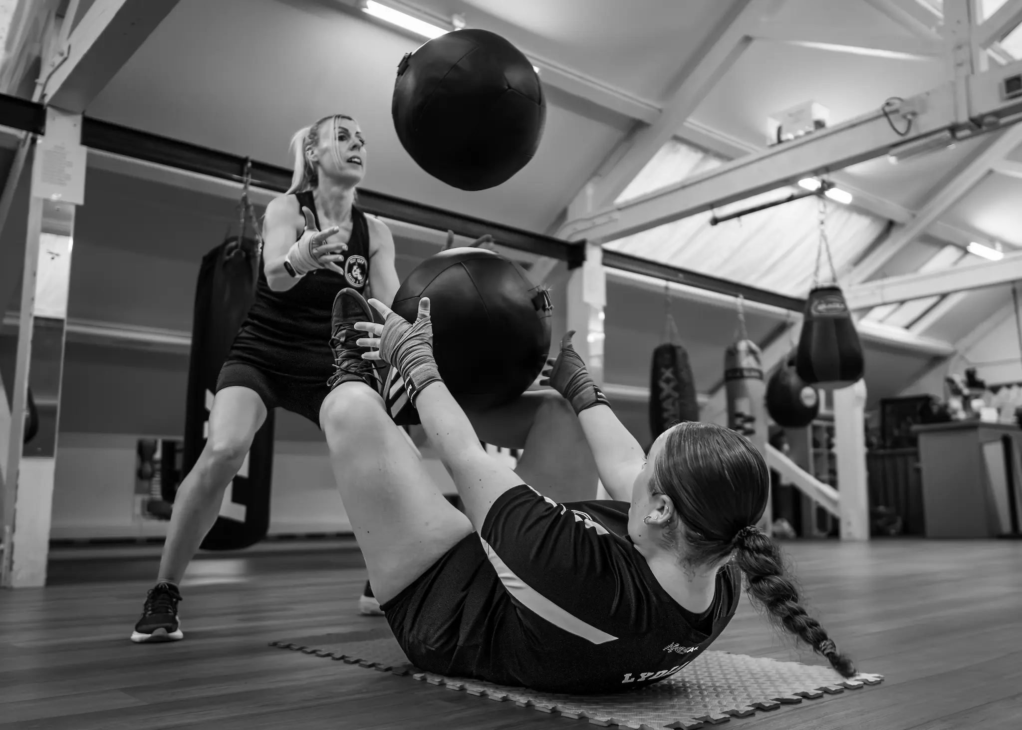 Women's Boxing Conditioning and Core Training at West Oxon Boxing wo women performing a medicine ball core workout on a gym mat, with one athlete throwing a ball and the other catching it while performing a sit-up.