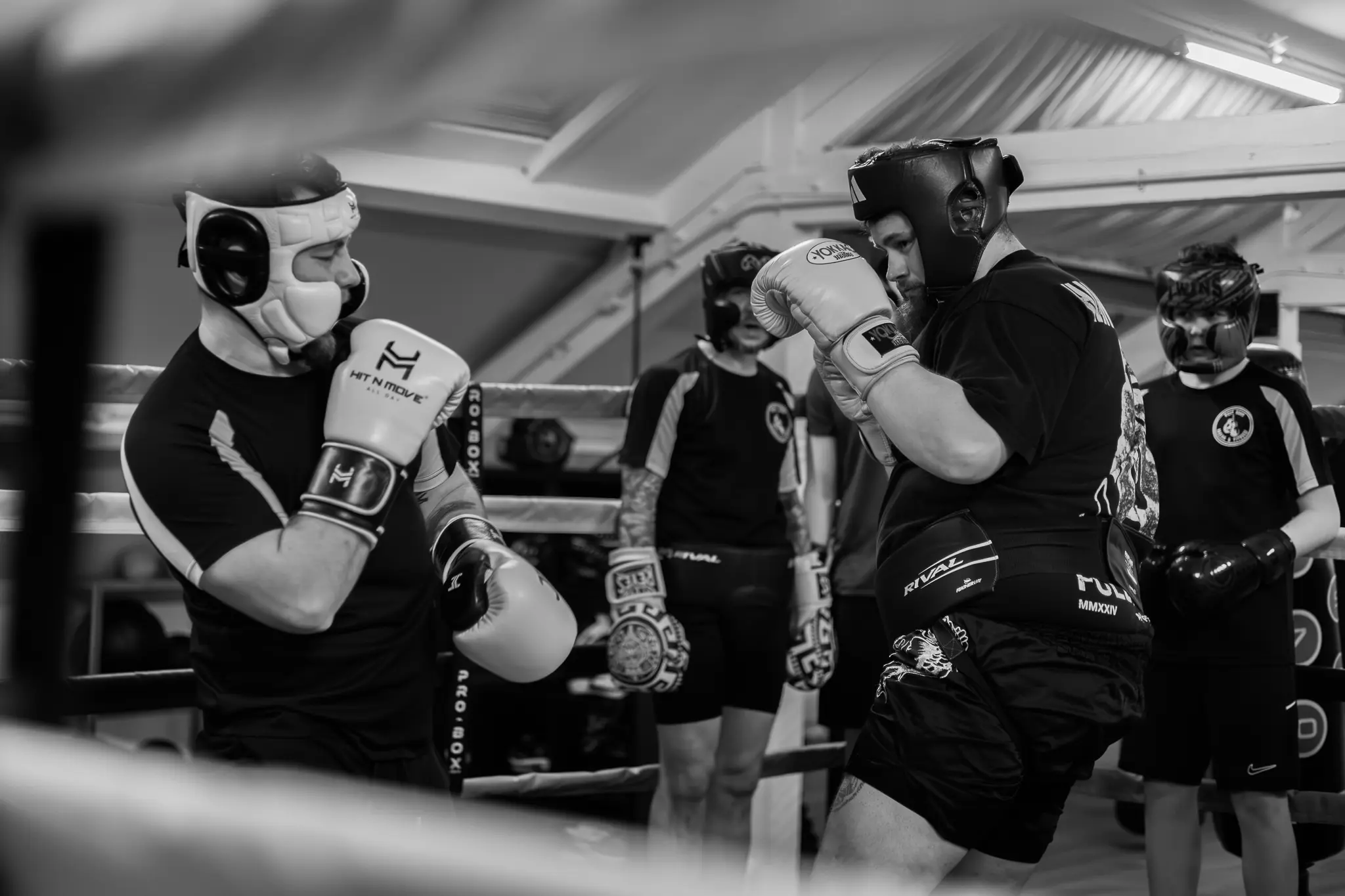 Two boxers in headguards and gloves engaging in technical sparring while a coach observes in the background at West Oxon Boxing.