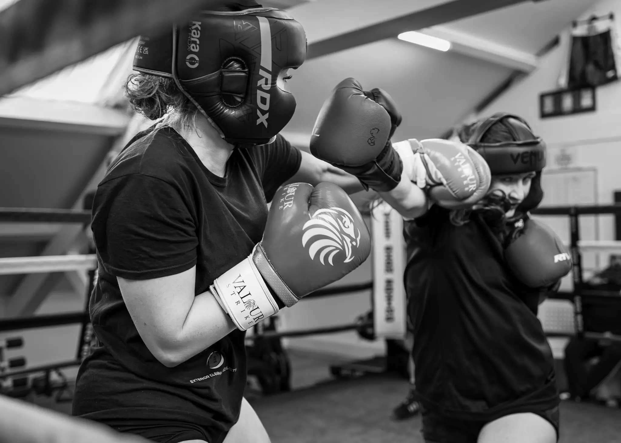 adies Boxing Sparring Witney Two female boxers in full protective gear engaging in a competitive technical sparring session in the ring.